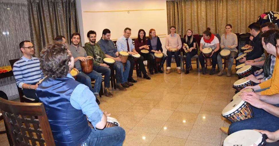 Participanți cântând la tobe la Drumming, o activitate de aliniere team building.