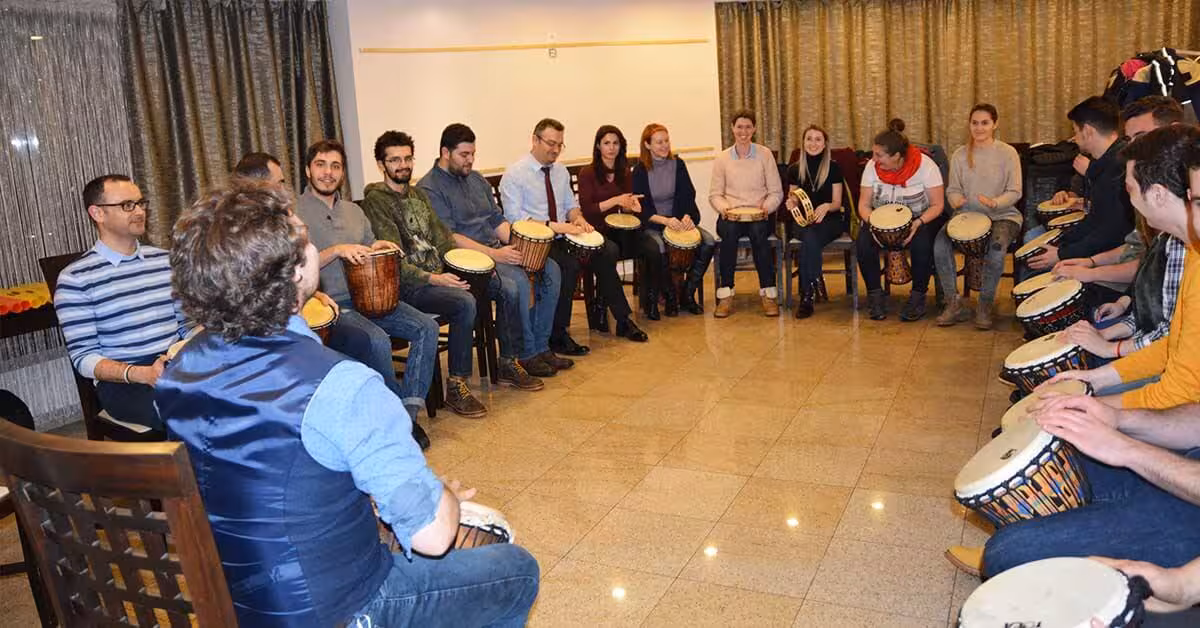 Participanți cântând la tobe la Drumming, o activitate de aliniere team building.