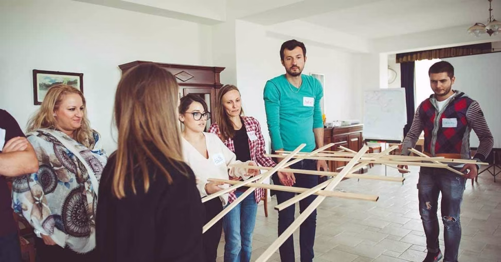 Echipă asamblând piese din lemn la Podul lui DaVinci, un exercitiu de logica team building.