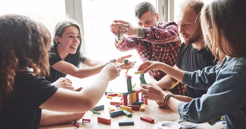 Grup de angajați relaxați colaborând la un joc de construit din lemn, un exemplu pozitiv de activitate pentru a evita cele mai frecvente greșeli în team building.